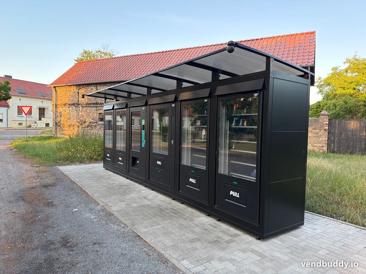 A row of 24/7 outdoor vending machines under a canopy on private land beside a building, placed with the property owner's permission