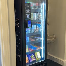 Locked glass-front 24-hour smart vending cooler installed in a building hallway