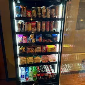 Lit snack and drink cooler standing against dark wood paneling next to a bar rail