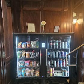 Two-door glass front cooler built into an ornate wood-paneled lobby wall beside a staircase