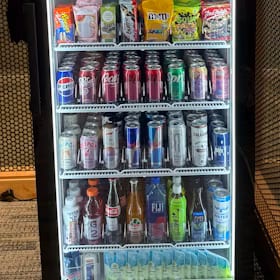 Glass-front cooler stocked with rows of energy drink cans, waters and bottled drinks