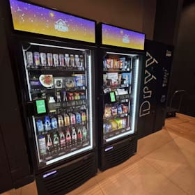 Two lit smart coolers with illuminated header screens standing in a dark entertainment venue