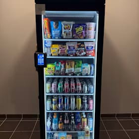 Newly installed glass-front smart cooler standing level against a tiled lobby wall, fully stocked and lit