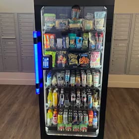 Glass-front smart cooler with a lit blue handle standing beside apartment mailboxes