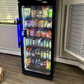 Stocked glass-front cooler installed next to a bank of apartment mailboxes on a wood-look floor