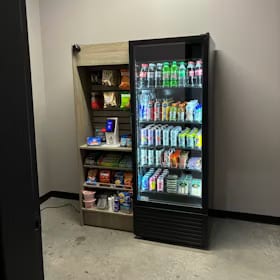 Small micro market corner with a glass-front drink cooler beside open snack shelving