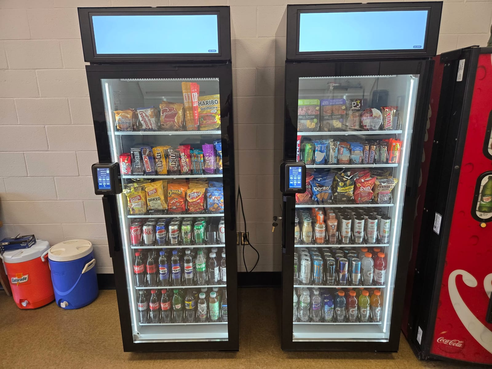 Two modern smart coolers installed beside an older legacy vending machine in an office break room