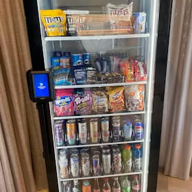 Glass-front drink cooler with candy and chip bags merchandised across the upper shelves above rows of cans and bottles